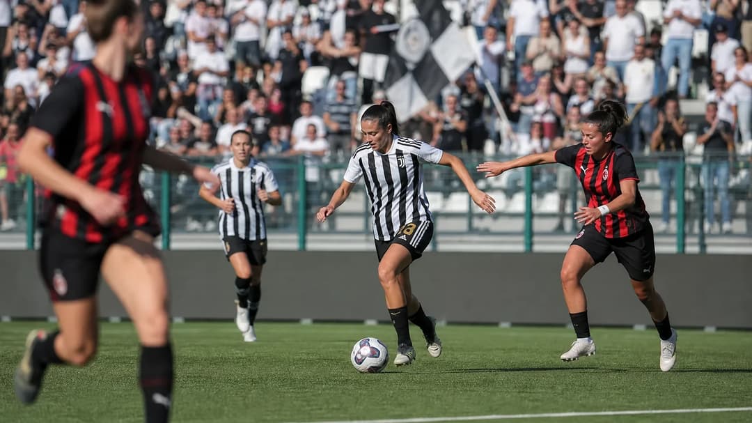 A wide shot of female football players from Juventus Women and AC Milan competing fiercely on a football pitch in Biella.