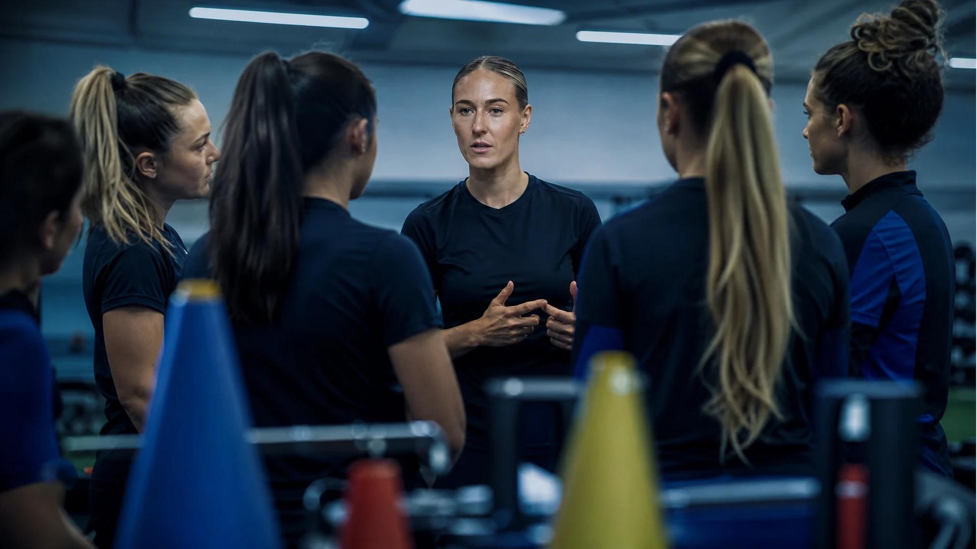 Emma Kullberg and teammates in a football training facility, engaged in a conversation.