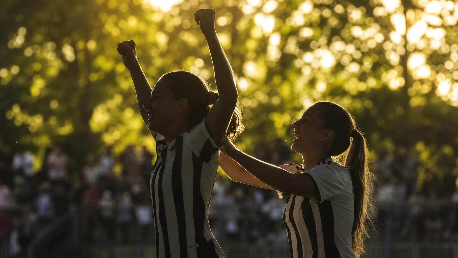 Silhouette of two female football players celebrating in sunlight.