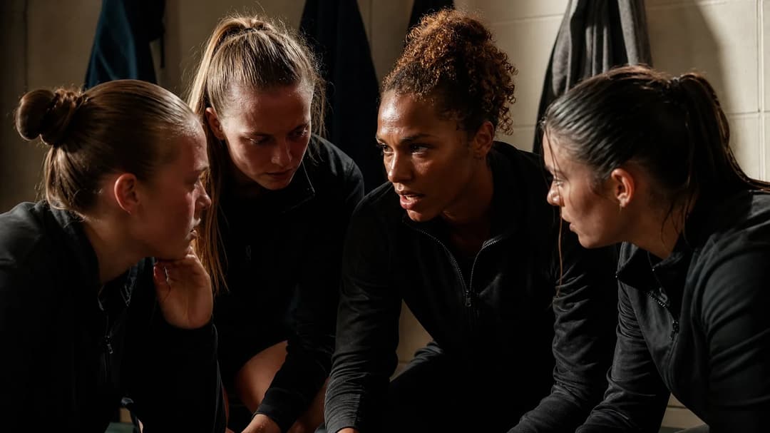 Four female football players in a tense discussion in a changing room.