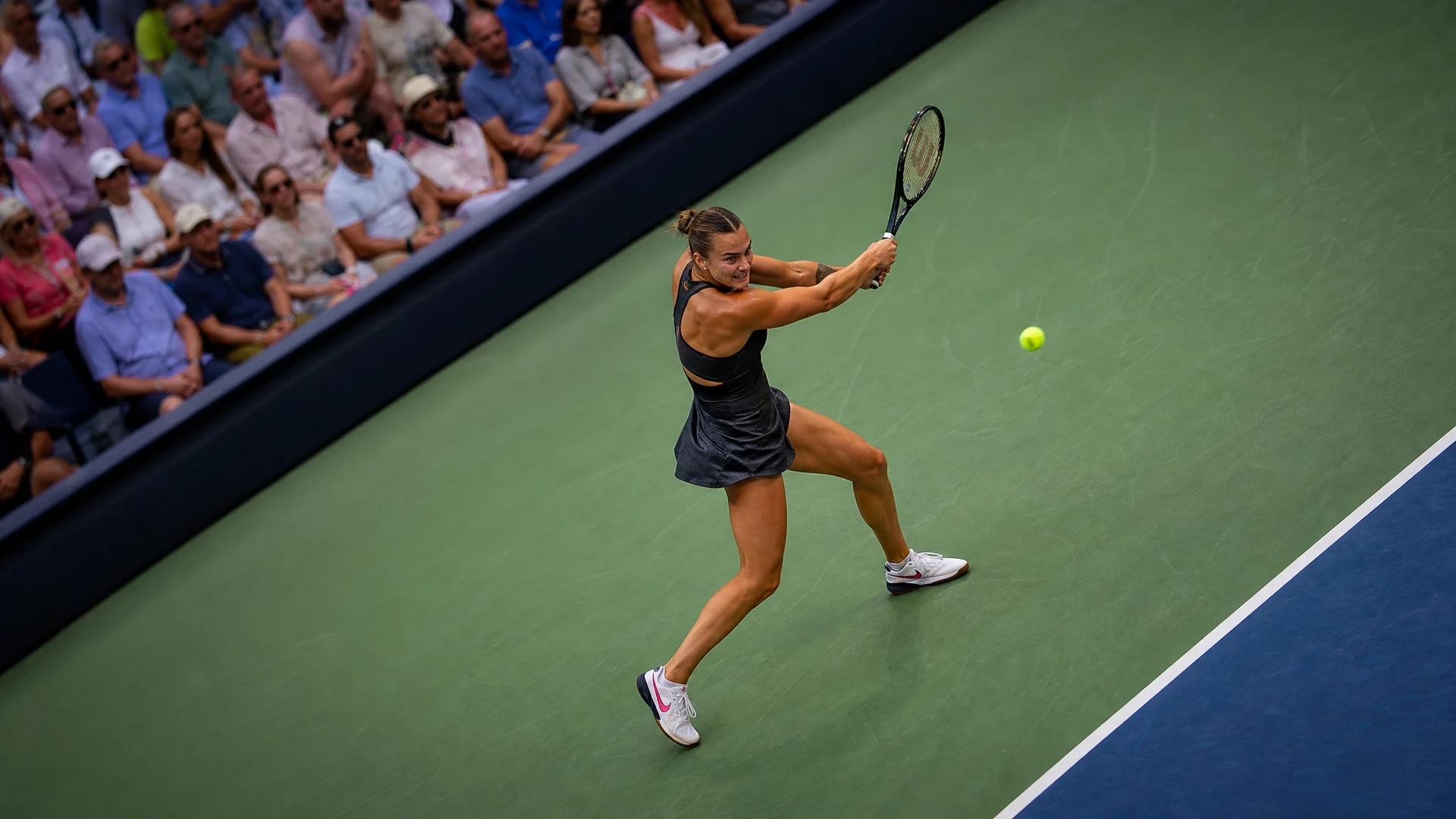 Aerial view of Aryna Sabalenka executing a backhand shot at the US Open, surrounded by a vibrant crowd.