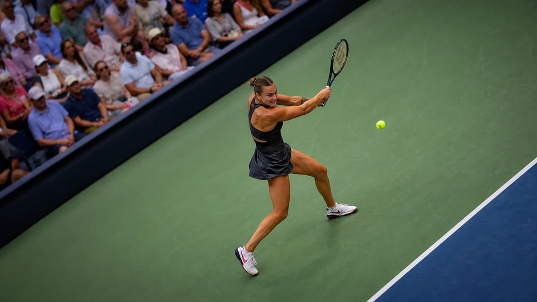 Aerial view of Aryna Sabalenka executing a backhand shot at the US Open, surrounded by a vibrant crowd.