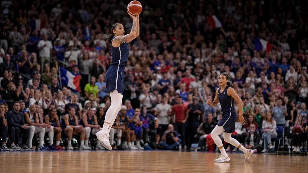 A basketball player jumps to take a shot during a game, surrounded by an enthusiastic crowd.