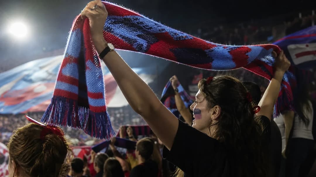 A female fan of the Boston Independent Supporters' Association cheers with a vibrant scarf in an over-the-shoulder view.