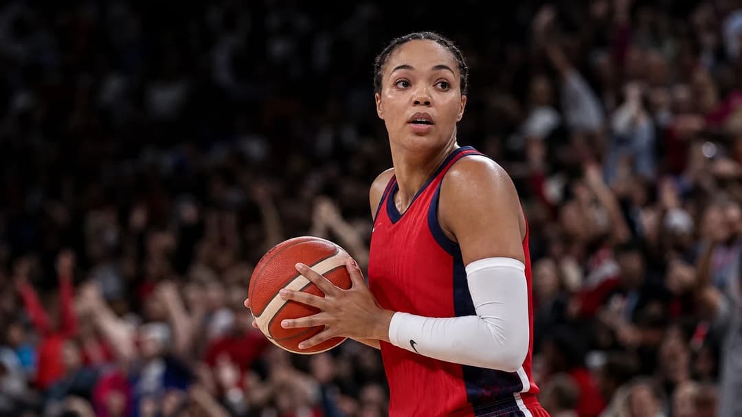 A basketball player stands out in a spotlight on the court, with a vibrant crowd in the background.