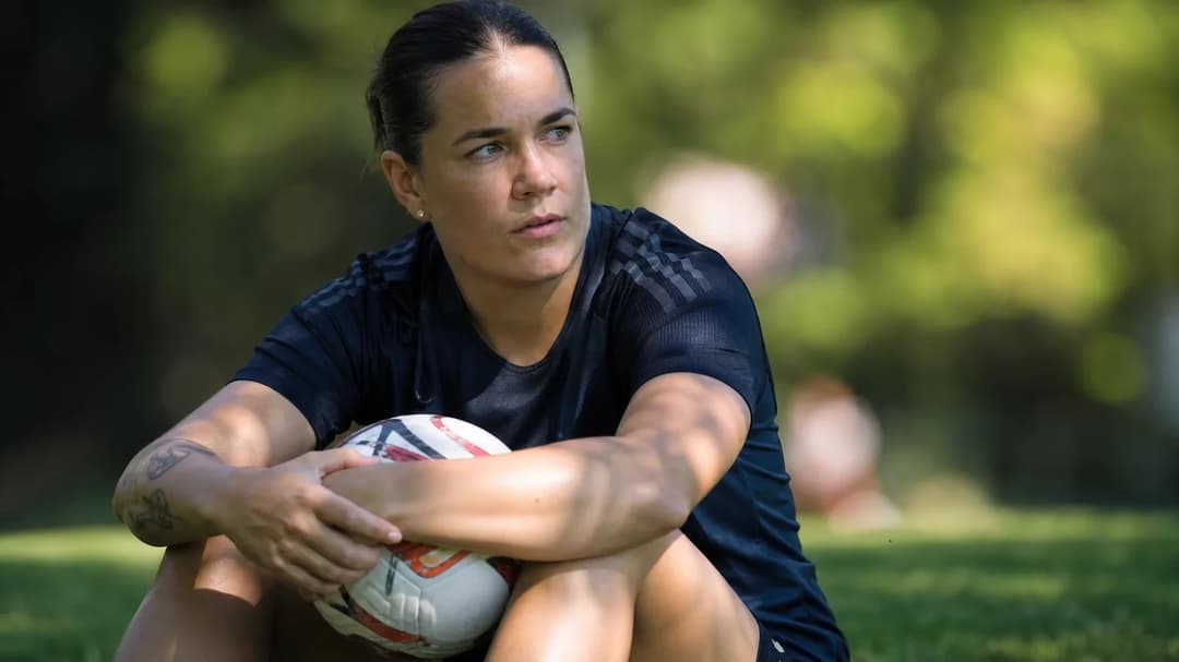 A close-up of a female football player, Lisa Baum, sitting on grass with a soccer ball, bathed in dappled sunlight.