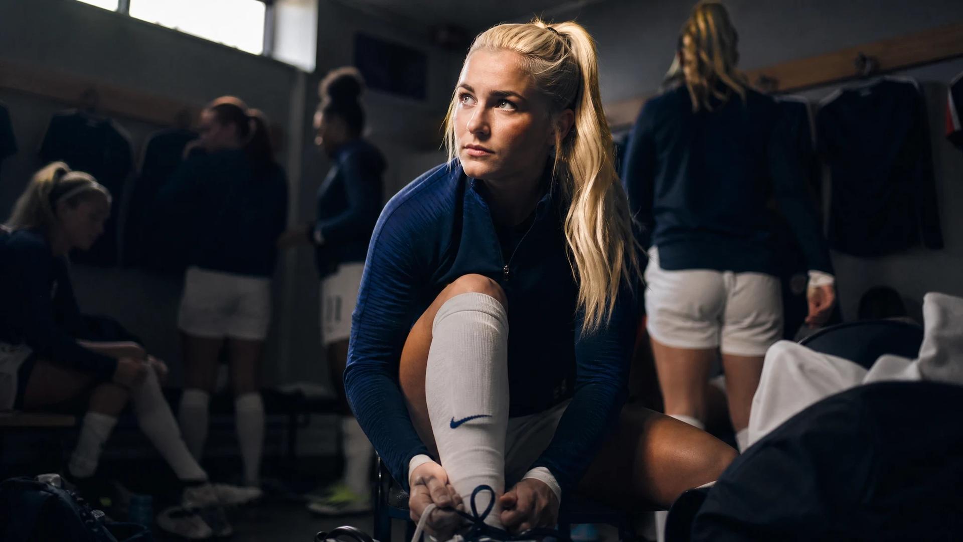 Laura Blindkilde Brown tying her shoelaces in a locker room, focused and determined.