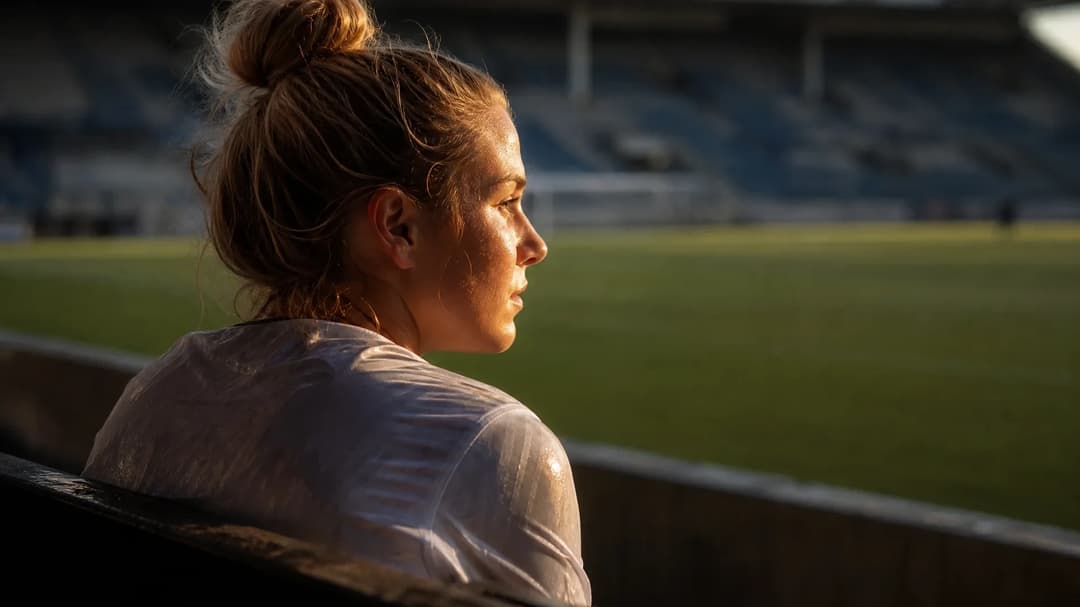 A young female footballer reflecting on an empty training pitch.